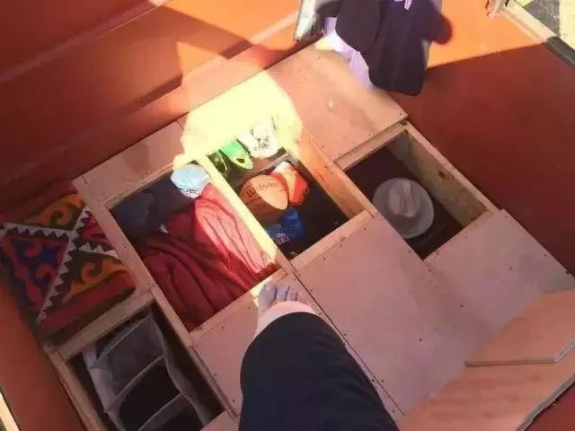 Vista des d\'un compartiment de magatzem ple de roba doblada, bosses i un barret, en tons càlids taronja